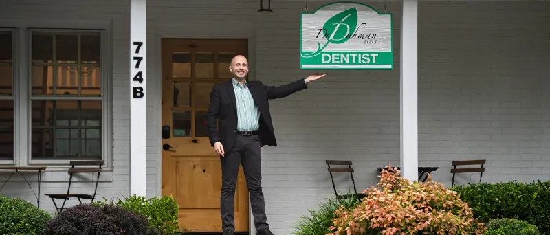 Dr. Dahman in front of dental office under sign smiling